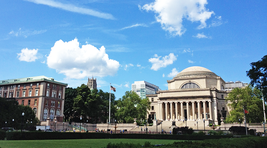 View of Dodge Hall and Low Library from the South Lawn, with a bright blue sky and clouds overhead