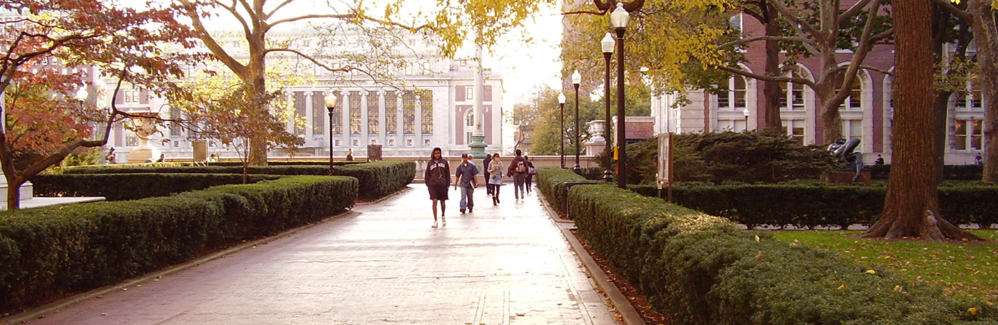 Students walking on a path bordered by hedges, with Butler Library in the far distance