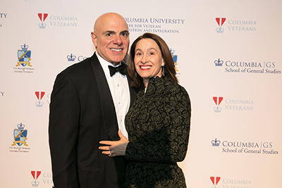 A man and woman pose in front of the step-and-repeat, which displays logos of the Military Ball host organizations