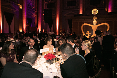 Guests sitting at their table enjoy conversation; in the background, a large Columbia University Crown is projected onto the wall