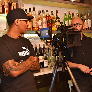 C. Craig Patterson and a cameraman on the set of LIV, standing behind a bar with liquor bottles in behind them