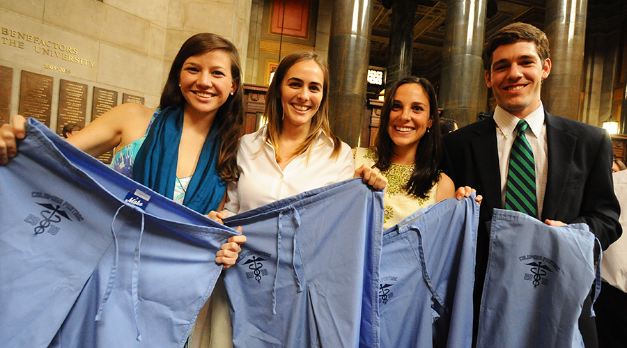 Four students show off the scrubs they received in honor of completing the Columbia University Postbac Premed Program