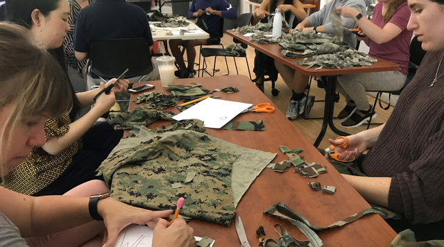 Three students craft their artwork from military uniforms while sitting at a table. 